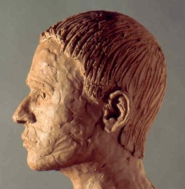 Clay sculpture of a human head. View is side profile.